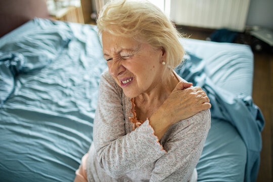 Senior woman wincing with shoulder pain in bedroom