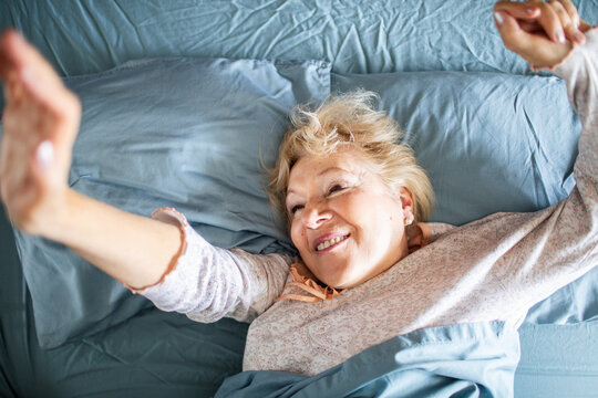 Senior woman smiling and stretching in bed at home