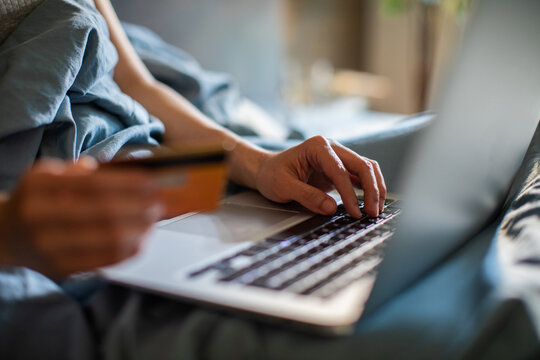 Person shopping online with credit card on laptop in bed at home