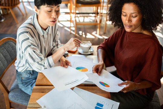 Two colleagues reviewing financial charts at a coffee shop