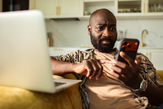 Concerned man checking smartphone on sofa at home