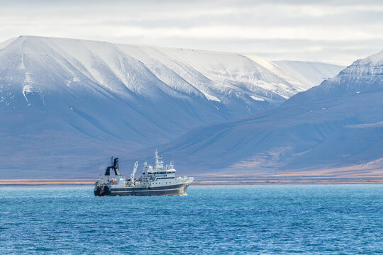 Remote maritime landscape with a ship on cold blue water below steep snowy mountains and broad treeless Arctic valley, Spitsbergen, Svalbard, Norway