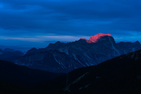 Tofana di Rozes catches the last pink alpenglow above dark mountain ridges during blue hour in the Italian Dolomites near Cortina d'Ampezzo. Colors: blue, pink, black.