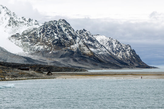 Dramatic Arctic coastal landscape with steep snow-covered mountains, broad shoreline and cold fjord water during summer, Spitsbergen, Svalbard, Norway