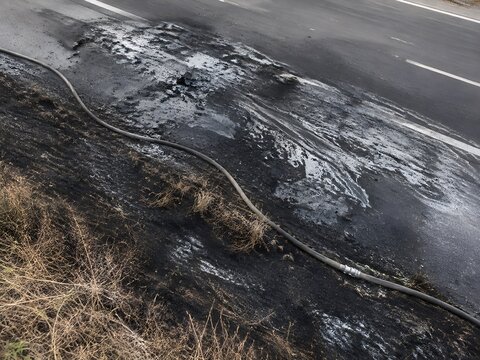 Scorched tarmac and burnt grass verge where a vehicle fire was extinguished