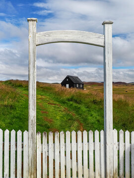 White wooden fence in the foreground and small black church visible in the distance. Kr&yacute;suv&iacute;k or Kr&iacute;suv&iacute;kurkirkja church in the Reykjanes Peninsula, Iceland. Symbol of heritage Icelandic identity.