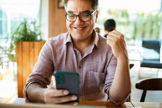 Happy man celebrating good news on smartphone at cafe