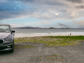 Gray car parked near beach. Ocean waves crash on rocky shore. Distant hills under cloudy sky. Quiet coastal scene with no people. Ideal for travel, adventure, or automotive themes © mark_gusev