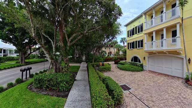 4K walking video moves beneath banyan trees beside yellow townhouses and gardens in Naples, Florida.