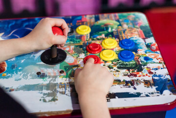 Child hands playing on vintage arcade machine control panel with joystick and buttons © Matico