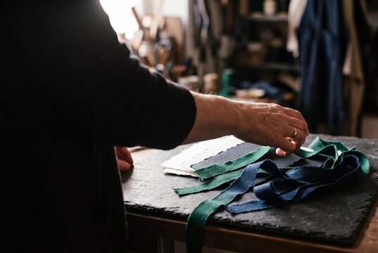 Craftsman selecting fabric swatches and ribbon trims on a slate table in a workshop