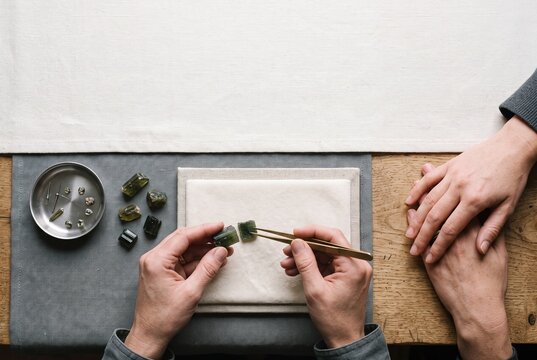 Jeweler examining rough green tourmaline gemstones with tweezers on a workshop table during a client consultation