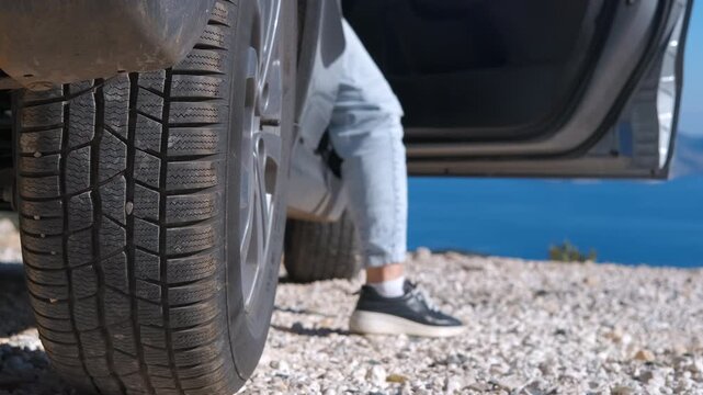 Person getting out of car at scenic sea viewpoint. Close-up of a person's legs getting out of a car parked, stopping to enjoy the beautiful ocean view during a summer road trip adventure