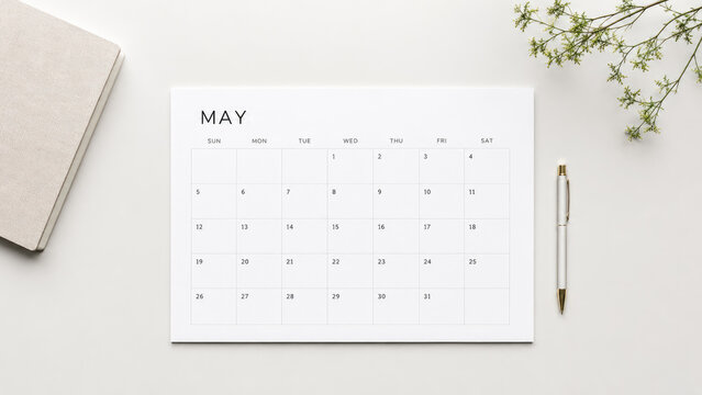 Minimal flat lay of a May calendar page on a white desk with pen, notebook and a small sprig of greenery for planning and organization