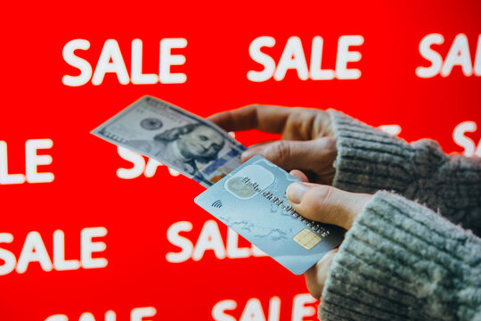 Person holding US dollar banknotes and a bank card during sale shopping.