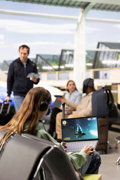 Excited gamer plays an online competition game in an airport terminal while waiting for a flight, combining travel downtime with strategy and entertainment.