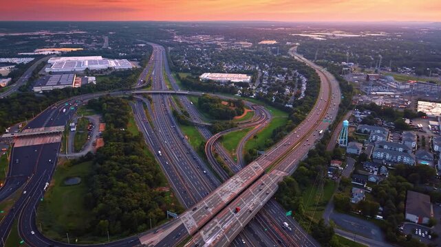 Huge modern interchange crossing the green cityscape. Massive road system in the city at sunset time. Aerial view.