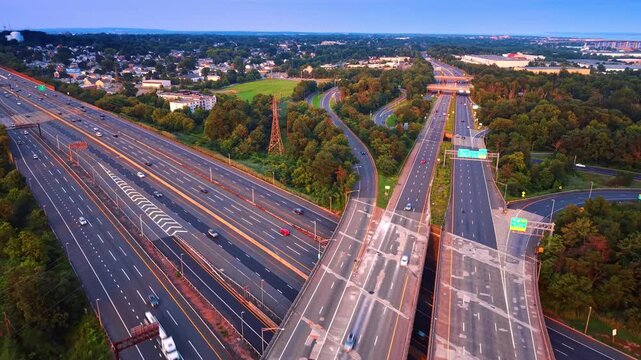 Concrete overpass over the parallel multi-lane highways. System of motorways along the green forests and cityscape. Aerial view.