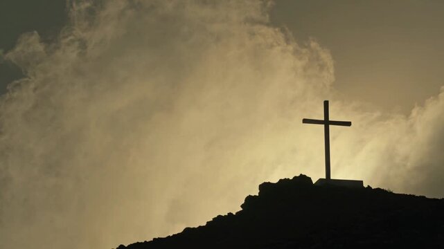 Silhouette of a single wooden cross on a hill against dramatic cloudy sky