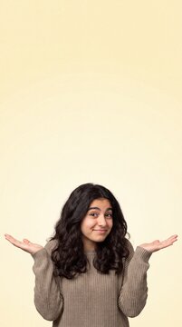 Teenage girl shrugging shoulders with hands open, showing confusion or uncertainty against a light beige background