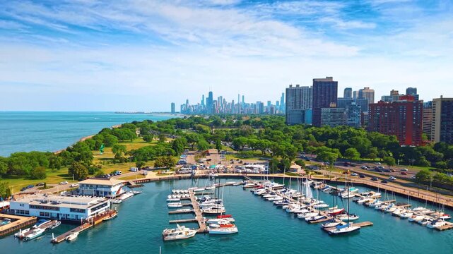 Sailboats at Belmont Harbor with Chicago skyline. An elevated view shows rows of moored boats, a clubhouse and lakeside towers beneath a clouded sky.