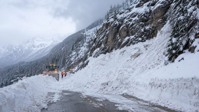 Snowplow and workers clearing avalanche debris on a mountain highway in a snowy winter landscape