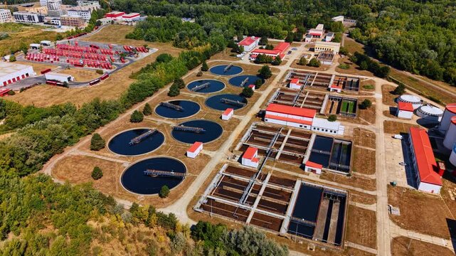 Wastewater purification station with dark sedimentation basins. High angle drone photograph captures water treatment tanks and red buildings in daylight.