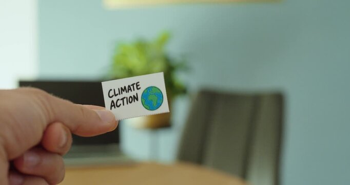 Close-up of a hand holding a &ldquo;Climate Action&rdquo; card with Earth symbol, representing climate protection, sustainability and environmental responsibility.