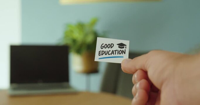 Close-up of a hand holding a &ldquo;Good Education&rdquo; card with graduation cap symbol, representing learning, knowledge and educational opportunities.