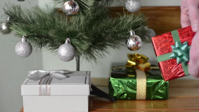 Man's hand picking up a wrapped gift from under a Christmas tree