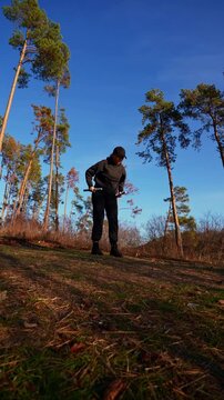 Young adult woman exercises with adjustable metal dumbbells during outdoor strength workout near lakeside. Person wears black sportswear and cap while performing arm exercise in autumn landscape under