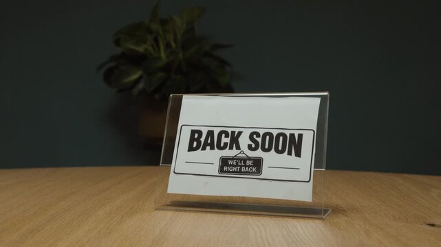 Man places a &ldquo;Back Soon&rdquo; sign on the desk, representing a temporary absence, short break, closed service and returning shortly.