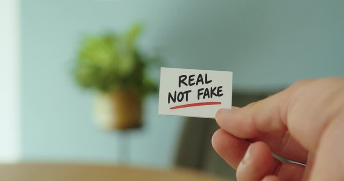 Close-up of a hand holding a &ldquo;Real Not Fake&rdquo; card, representing authenticity, truth, credibility and genuine information.