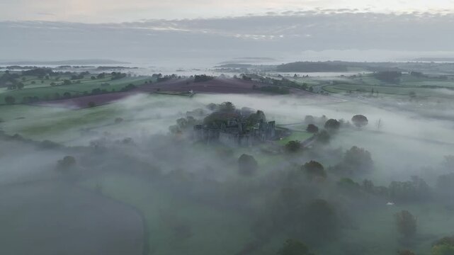 Raglan Castle in the fog at dawn from a drone, Monmouthshire, Wales, England, United Kingdom