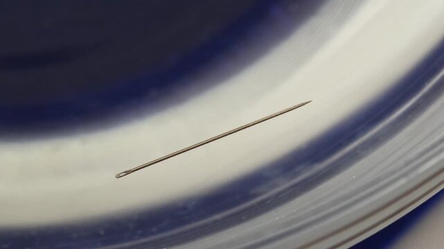 Metal sewing needle floating in water in a glass container.