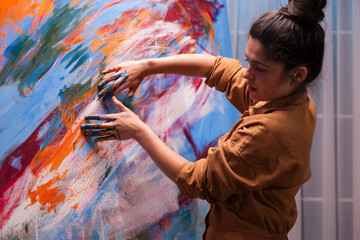 Woman artist presses both paint-covered hands against an abstract canvas, combining direct touch, bold color and expressive movement in her creative process. © DC Studio