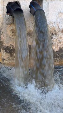 Environmental pollution clip showing dirty sewage water gushing out of two large pipes into a canal.
