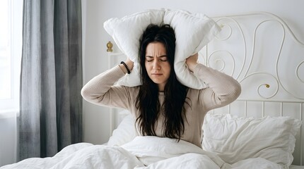 Fototapeta premium Stressed Young Woman Covering Ears with Pillow to Block Loud Noise in Bright Bedroom, Concept of Insomnia, Migraine, Sleep Disorder, and Morning Annoyance in Domestic Setting