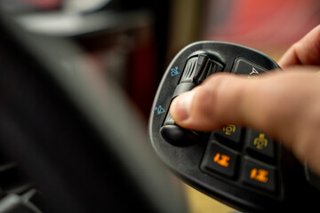 Hand of operator pressing button on multifunctional ergonomic joystick control lever inside cabin of modern agricultural or industrial machinery. © Marina