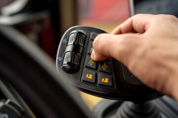 Hand of operator pressing button on multifunctional ergonomic joystick control lever inside cabin of modern agricultural or industrial machinery. © Marina