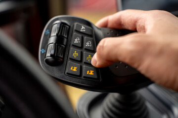 Hand of operator pressing button on multifunctional ergonomic joystick control lever inside cabin of modern agricultural or industrial machinery. © Marina