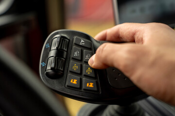 Hand of operator pressing button on multifunctional ergonomic joystick control lever inside cabin of modern agricultural or industrial machinery. © Marina