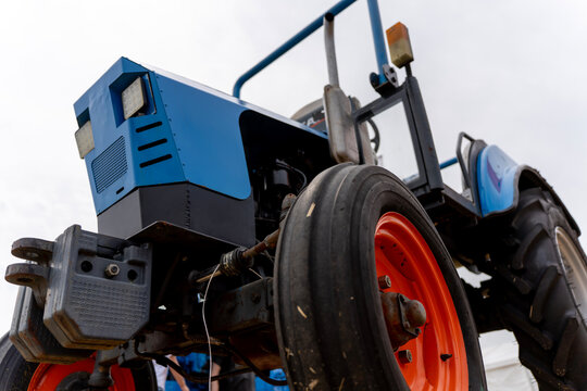Low angle view of blue agricultural tractor with bright orange wheels and front ballast weight against overcast sky outdoors.