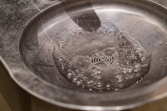 Water flowing from a drinking fountain with bubbles in a metal basin