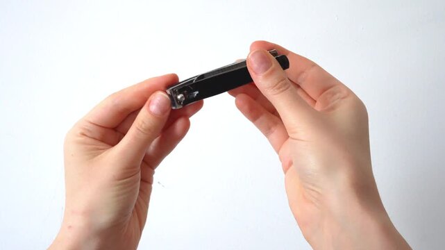Woman cutting fingernails with steel clipper tool against white background. Daily personal care and hygiene concept. Minimalist video of hand grooming routine.