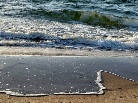 Foam of a breaking wave spreading over wet sand in the evening light