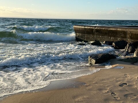 Concrete breakwater and dark rocks with waves breaking on a beach
