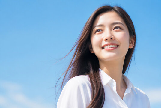 青空の下で上を向いて微笑む若い女性