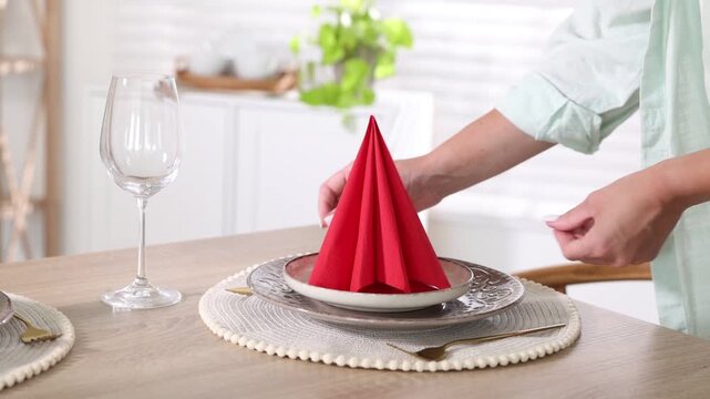 Woman arranging folded napkin and dishware onto wooden table indoors, closeup