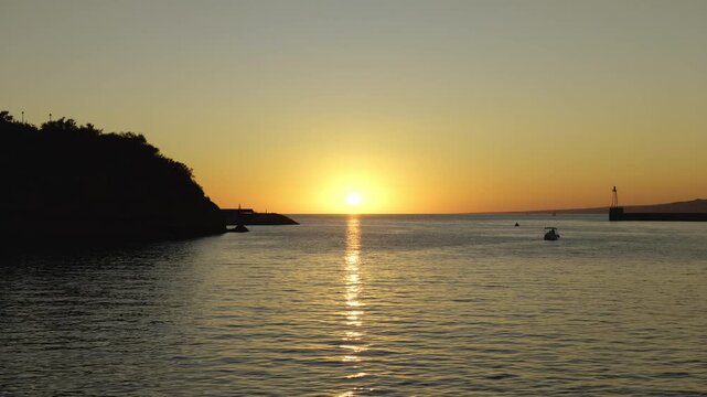 Golden sunset reflecting on the calm sea at the entrance of a harbor in Marseille, France